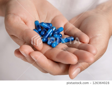 Cupped female hands with a pile of blue medical herbal capsules closeup over white shirt Cupped female hands with a pile of blue medical herbal capsules closeup over white shirt 126364028