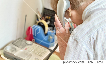 Elderly woman's hand holding a landline telephone receiver to her ear Elderly woman's hand holding a landline telephone receiver to her ear 126364251