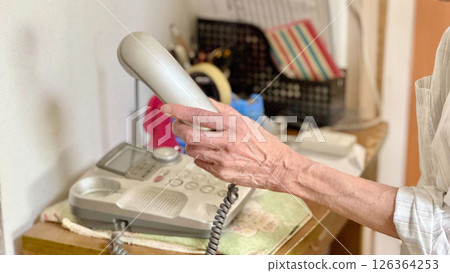 The hand of an elderly woman holding a landline telephone receiver 126364253
