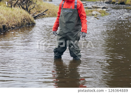A man in a fishing suit stands in a river A man in a fishing suit stands in a river 126364889