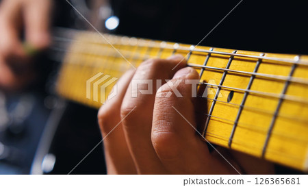 Macro shot of the guitarist's fingers pressing against the bright yellow fretboard. Guitarist playing a meta riff on an electric guitar. 126365681