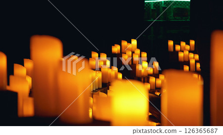 A close-up of numerous lit candles in a dark environment. The background is blurred and orange. A close-up of numerous lit candles in a dark environment. The background is blurred and orange. 126365687