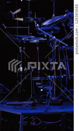 Close-up of a drum kit and a drummer behind it on a dark stage with blue lighting. The background is blurred. Close-up of a drum kit and a drummer behind it on a dark stage with blue lighting. The background is blurred. 126365688