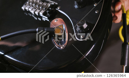 Close-up of an electric guitar's input jack and volume knob on a glossy black body. The chrome hardware and instrument cable create reflective highlights against the dark finish. 126365964
