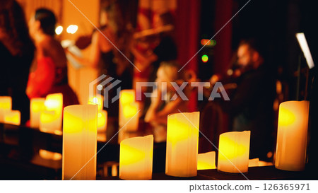 A close-up of a row of lit candles in the foreground with a blurred background of a musical performance. Candlelight concert. A close-up of a row of lit candles in the foreground with a blurred background of a musical performance. Candlelight concert. 126365971