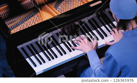 Pianist in blue clothes playing piano, hands resting on white keys. Naked copper-coloured piano strings and tuning pins. Top view. Pianist in blue clothes playing piano, hands resting on white keys. Naked copper-coloured piano strings and tuning pins. Top view. 126365976