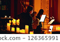 A dimly lit concert scene with musicians playing string instruments, illuminated by numerous glowing candles, creating a warm and intimate atmosphere. 126365991