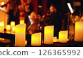 Close-up of a row of lit candles in the foreground with a blurred background of a musical performance. Chamber music concert by candlelight. 126365992