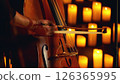 Close-up of a musician playing the double bass on a stage surrounded by candles. 126365995