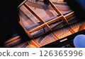 A close-up of the inside of a grand piano, showing the strings and hammers. A person's hand and a blue hat are visible in the foreground. Top view. 126365996