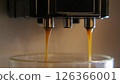 A close-up of an espresso machine with two spouts pouring espresso into a glass cup. The espresso is a dark brown color and is dripping into the cup. 126366001