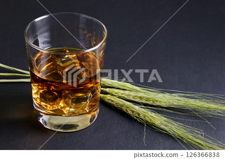 glass of whiskey with ice and ears of rye on a black stone table 126366838