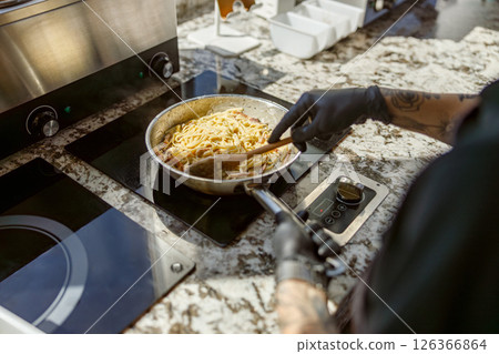 A skilled chef is cooking pasta in a beautifully designed and modern kitchen environment 126366864