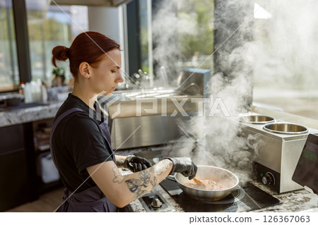 A skilled chef is actively cooking in a modern kitchen filled with steam and delicious aromas A skilled chef is actively cooking in a modern kitchen filled with steam and delicious aromas 126367063