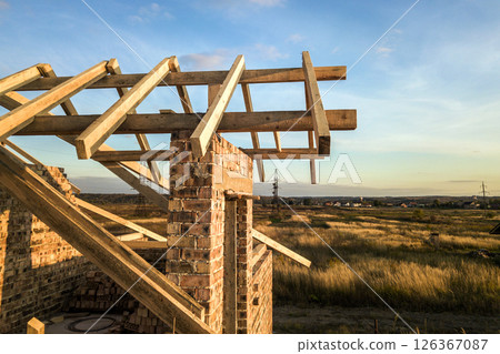 Private residential house with wooden roof frame structure under construction. Unfinished brick building under development. Private residential house with wooden roof frame structure under construction. Unfinished brick building under development. 126367087