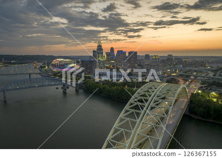 Night urban landscape of downtown district of Cincinnati city in Ohio, USA. Skyline with driving cars on bridge and brightly illuminated high skyscraper buildings in modern American megapolis Night urban landscape of downtown district of Cincinnati city in Ohio, USA. Skyline with driving cars on bridge and brightly illuminated high skyscraper buildings in modern American megapolis 126367155