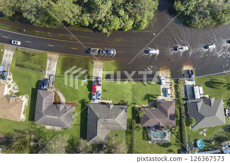 Flooded american street with moving vehicles and surrounded with water houses in Florida residential area. Consequences of hurricane natural disaster 126367573