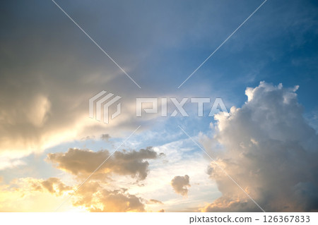 Dramatic sunset landscape with puffy clouds lit by orange setting sun and blue sky. 126367833