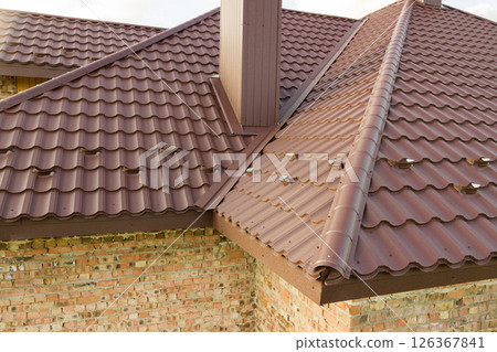 Detail of house roof structure covered with brown metal tile sheets. Detail of house roof structure covered with brown metal tile sheets. 126367841