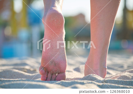 Close up of female feet walking barefoot on white grainy sand of golden beach on blue ocean water background Close up of female feet walking barefoot on white grainy sand of golden beach on blue ocean water background 126368010