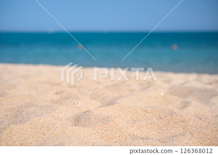 Close up of clean yellow sand surface covering seaside beach with blue sea water on background. Travel and vacations concept. 126368012