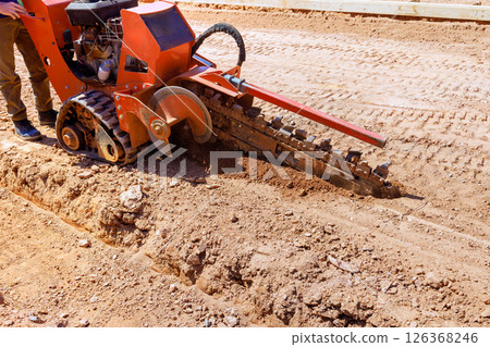 Worker uses trencher to dig seam for underground utilities at construction site. Worker uses trencher to dig seam for underground utilities at construction site. 126368246