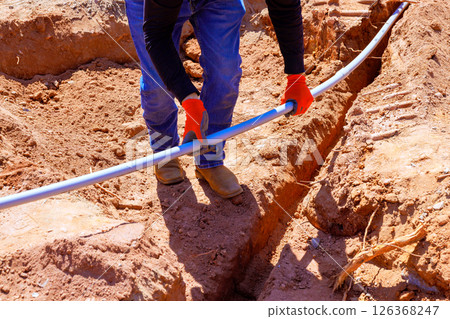 Construction worker lays electrical pipe in filled trench during foundation work 126368247