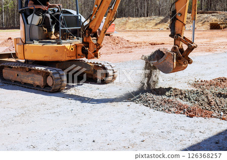 Heavy machinery operator uses an excavator to digs trench, move gravel at construction site 126368257