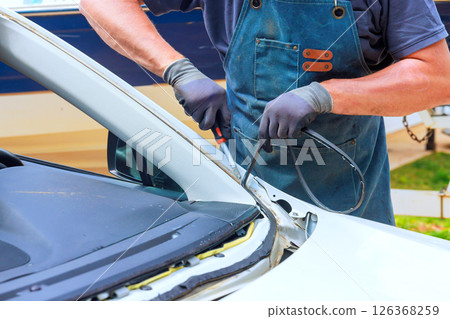 Skilled technician works on vehicle trim removes damaged silicone at car in auto repair shop for replacements windshield 126368259