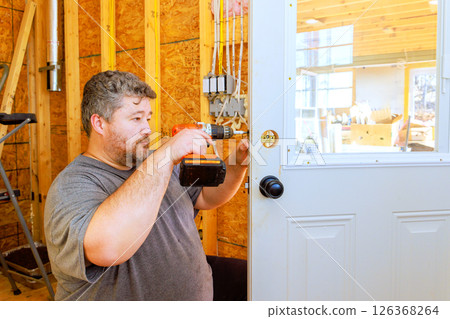 Craftsman carefully attaching doorknob in wooden works filled with tools materials during construction 126368264