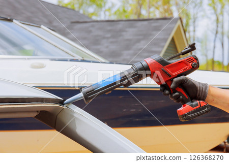 Worker is sealing windshield edge with caulking gun while repair vehicle 126368270