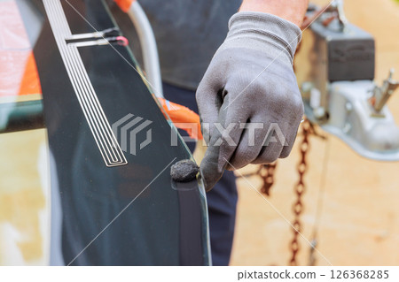 Worker wearing gloves meticulously fixes applies adhesive car windshield at workshop 126368285