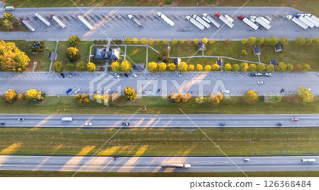 Big parking truck stop for tractor trailers rest area near busy American highway. Hauling cargo concept Big parking truck stop for tractor trailers rest area near busy American highway. Hauling cargo concept 126368484