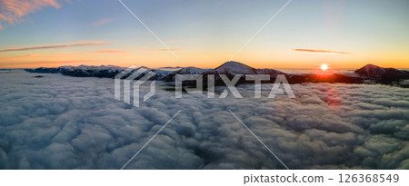 Aerial view of vibrant sunrise over white dense fog with distant dark Carpathian mountains on horizon. 126368549