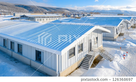 Snow-covered industrial buildings in winter landscape with blue sky and mountains. 126368697