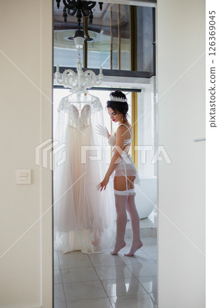 Seductive bride in a sexy lingerie and white stockings posing in a bathroom near her bridal dress 126369045