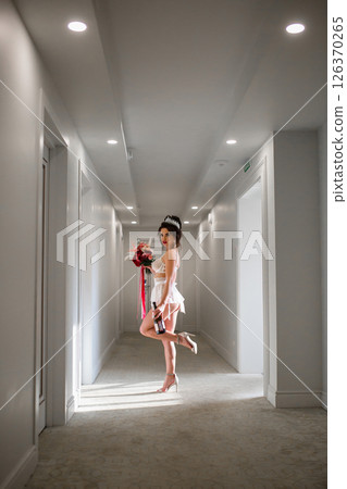 Seductive slender bride in a sexy lingerie posing in hotel corridor with bridal bouquet and bottle of wine 126370265