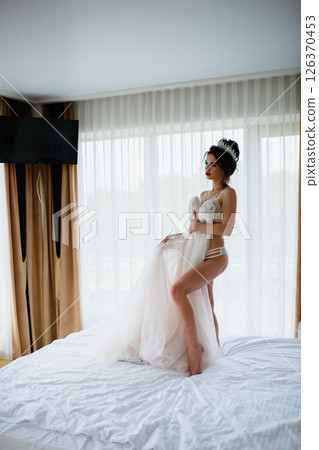 Seductive slender bride in a sexy lingerie posing in a hotel room with her bridal dress Seductive slender bride in a sexy lingerie posing in a hotel room with her bridal dress 126370453