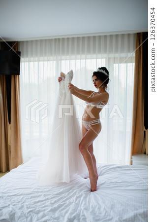 Seductive slender bride in a sexy lingerie posing in a hotel room with her bridal dress 126370454