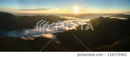 Aerial view of bright foggy morning over dark mountain forest trees at autumn sunrise. Beautiful scenery of wild woodland at dawn 126370462