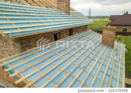 Aerial view of a brick house with wooden roof frame under construction. Aerial view of a brick house with wooden roof frame under construction. 126370496