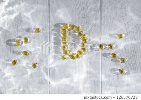 Yellow transparent capsules of vitamin d forming the letter d on a white wooden surface illuminated by sunlight, representing the importance of this vitamin for health and well-being 126370728
