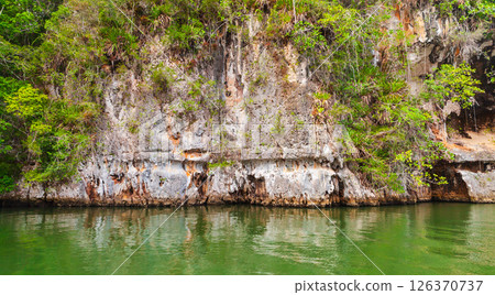 Samana bay view. A rocky cliff positioned by a tranquil green water Samana bay view. A rocky cliff positioned by a tranquil green water 126370737