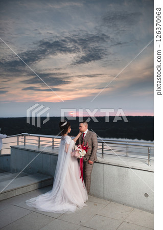 Young beautiful couple of newlywed posing in the evening against the background of an atmospheric panorama and stunning sunset Young beautiful couple of newlywed posing in the evening against the background of an atmospheric panorama and stunning sunset 126370968