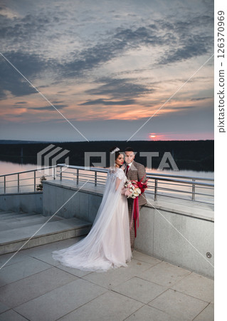 Young beautiful couple of newlywed posing in the evening against the background of an atmospheric panorama and stunning sunset Young beautiful couple of newlywed posing in the evening against the background of an atmospheric panorama and stunning sunset 126370969