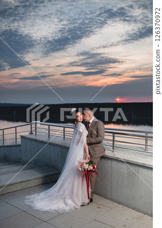 Young beautiful couple of newlywed posing in the evening against the background of an atmospheric panorama and stunning sunset Young beautiful couple of newlywed posing in the evening against the background of an atmospheric panorama and stunning sunset 126370972