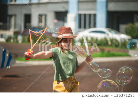 Cute school-age girl blows big soap bubbles in the courtyard of a multi-storey building 126371285