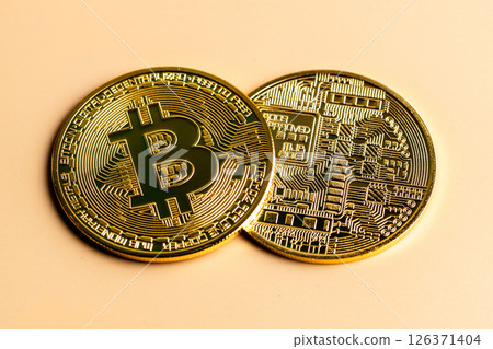 Two shiny gold bitcoin cryptocurrency coins rest on a beige background, showcasing both the front with the iconic b symbol and the back with intricate circuit-like details 126371404