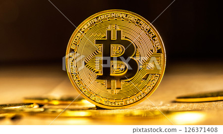 A single gold Bitcoin stands on edge on a wooden surface surrounded by scattered coins, creating a dramatic and luxurious visual representation of cryptocurrency and investment. 126371408