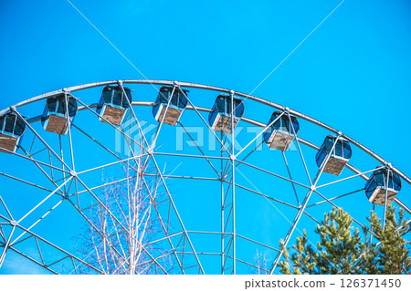 Ferris wheel with empty cabins offers breathtaking views over the amusement park, promising an exciting ride under the vast expanse of a vibrant blue sky Ferris wheel with empty cabins offers breathtaking views over the amusement park, promising an exciting ride under the vast expanse of a vibrant blue sky 126371450